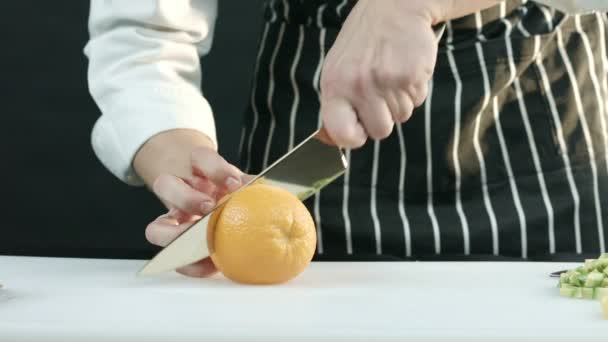 Homem corta uma laranja ao meio em um tabuleiro — Vídeo de Stock