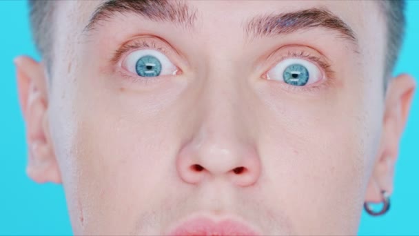 Close-up de um cara cara de cara em um fundo azul. Os olhos dele brilham — Vídeo de Stock