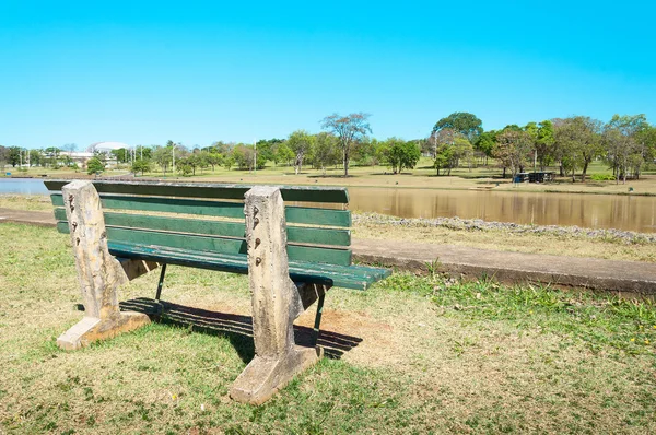 Green bench align to the left on a very peaceful place in a park with green vegetation and the lake.