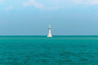 Denizin ortasında beyaz deniz feneri. Mavi deniz suyu ve mavi gökyüzü arka plan çevrili deniz feneri.
