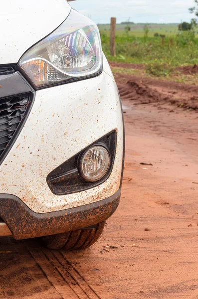 Front of a car on a farm road with mud everywhere.