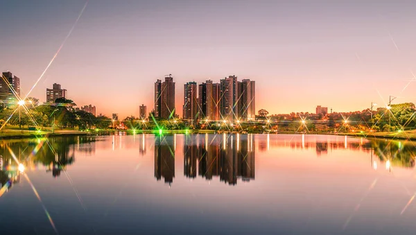 Pôr do sol em um lago de um parque com a cidade no fundo — Fotografia de Stock
