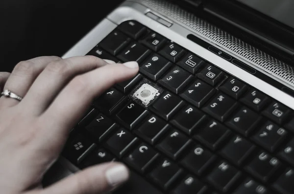 Hand of a woman over a laptop with a missing keyboard key.