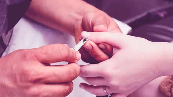 Manicurist using pliers to remove dead skin from around the clie
