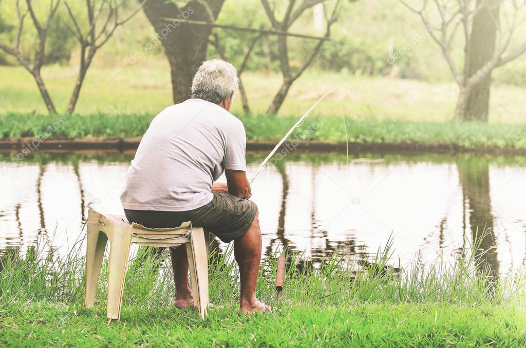 Retired old man seated next to the lake fishing and relaxing