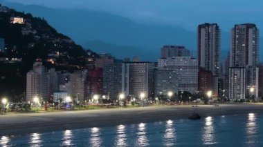 Alacakaranlıkta Paulista kıyısındaki bir Brezilya sahil şehrinin havadan görünüşü, şehrin ışıkları yanmaya başladığında. Praia do Itarare plajı, Sao Vicente Sp Brazil.