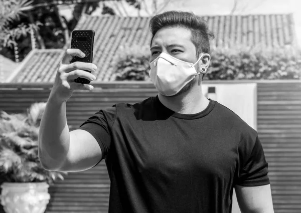 Yüz maskesi takan bir adamın portresi telefonda selfie çekiyor. Karantina sırasında izole edilmiş bir adam evde..