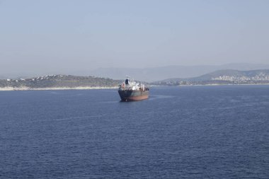Mavna yükleme için limana gidiyor. Uzaklarda küçük bir kasabanın evlerini ve dağlarını görüyoruz..