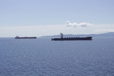 İki tanker yükleme için rıhtıma gidiyor. Arka planda, üzerinde beyaz bir bulut olan bir kıyı var..