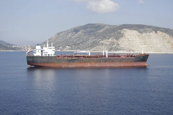 Tanker adanın kıyısına demir atmış, gövdesi pas içinde ve boyası soyulmuş, bu da eski bir gemi görüntüsü veriyor..