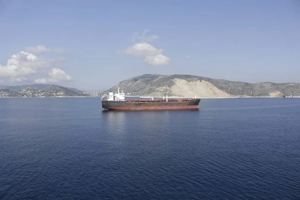 Tanker adanın kıyısına demir atmış, gövdesi pas içinde ve boyası soyulmuş, bu da eski bir gemi görüntüsü veriyor..