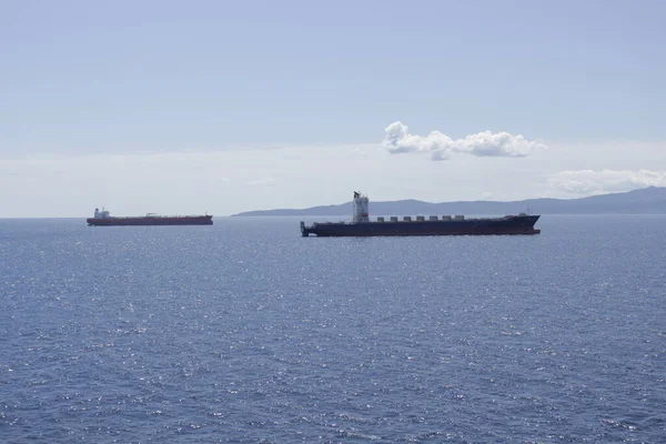 İki tanker yükleme için rıhtıma gidiyor. Arka planda, üzerinde beyaz bir bulut olan bir kıyı var..