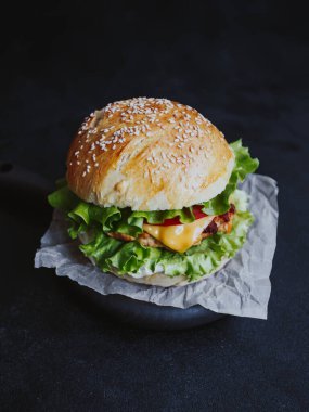 İştah açıcı taze ev yapımı burger, tavuk pirzolası, marul, domates, peynir ve sos. Siyah arka planda, tahta bir tahtanın üzerinde.