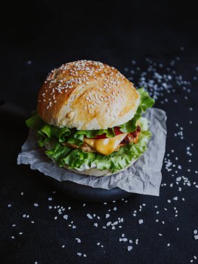 İştah açıcı taze ev yapımı burger, tavuk pirzolası, marul, domates, peynir ve sos. Siyah arka planda, tahta bir tahtanın üzerinde.