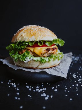 İştah açıcı taze ev yapımı burger, tavuk pirzolası, marul, domates, peynir ve sos. Siyah arka planda, tahta bir tahtanın üzerinde.