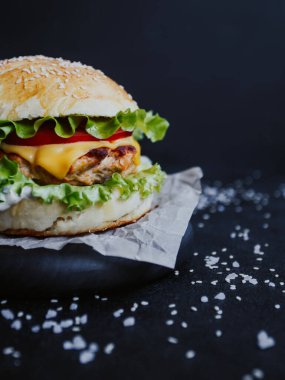 İştah açıcı taze ev yapımı burger, tavuk pirzolası, marul, domates, peynir ve sos. Siyah arka planda, tahta bir tahtanın üzerinde.