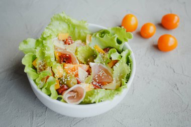 Taze marul, kiraz domatesleri, zeytin, güneşte kurutulmuş domates, Parma jambonu, çedar peyniri, parmesan, zeytin yağı ve susam. Sağlıklı yeme kavramı.