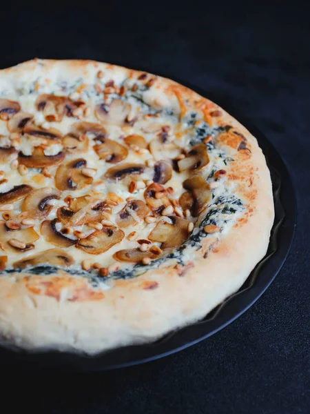 Homemade pizza with mushrooms, spinach, garlic, cream cheese and pine nuts, on a dark background.