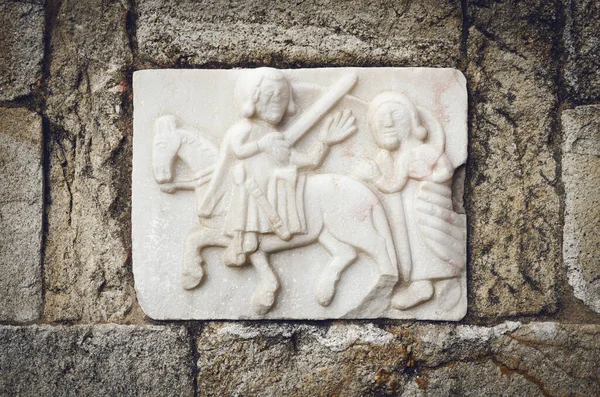 Gothic bas relief of Saint Martin of Tours on the external wall of a medieval church. Saint Martin is cutting half of his cloak with the sword to warm a poor beggar