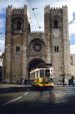 LISBON, PORTUGAL - 2 Şubat 2019: Lizbon, Portekiz 'in ortaçağ katedralinin önünden geçen geleneksel sarı elektrikli tramvay, 2 Şubat 2019 tarihinde turistlerin izlediği