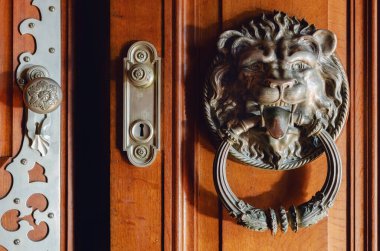 Lüks metal aslan şeklinde tokmak, eski bir ahşap kapıya dil uzatıyor.