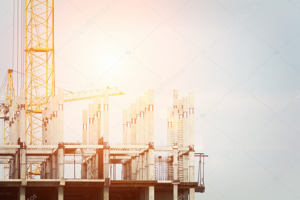 Construction crane and a building house against blue cloudy sky with sun