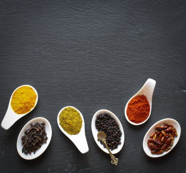 Siyah bir taş üzerinde kaşık içinde baharatlar 