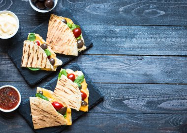 Delicious veggie quesadillas with tomatoes, olives, and cheddar cheese in a colorful dish over a wooden clipart