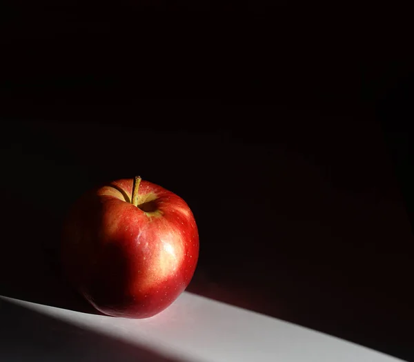 Красное яблоко на белом столе на черном фоне — стоковое фото