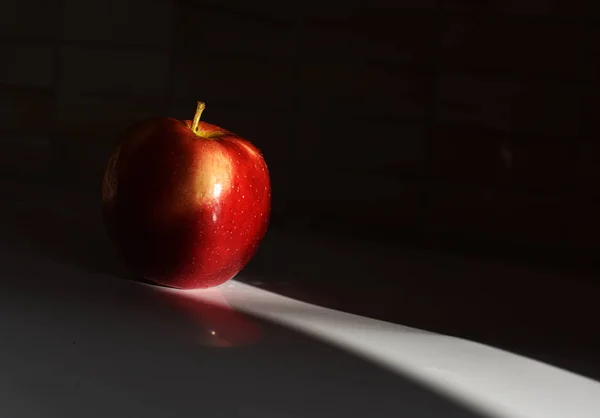 Una manzana roja sobre una mesa blanca sobre un fondo negro — Foto de Stock