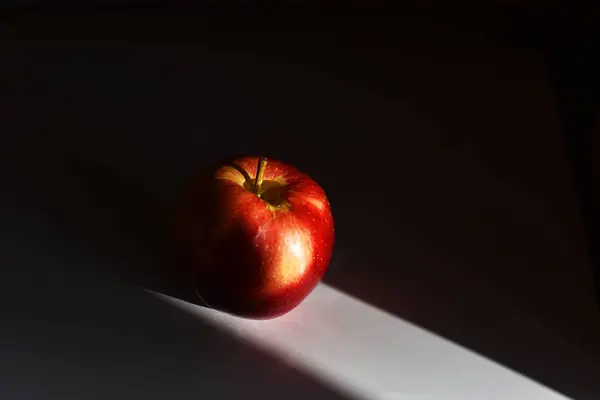 Una manzana roja sobre una mesa blanca sobre un fondo negro — Foto de Stock