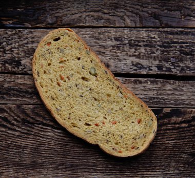 Tahta bir masanın üzerine mısır gevreği eklenmiş gri ekmek.