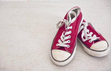 Beyaz lastik burunlu kırmızı spor ayakkabılar yıpranmış.