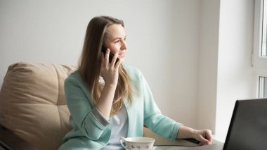 Bir kız telefonda dizüstü bilgisayarın yanında konuşuyor.