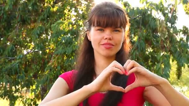 लड़की प्यार अवधारणा के रूप में पार्क में हाथों से दिल दिखाती है — स्टॉक वीडियो