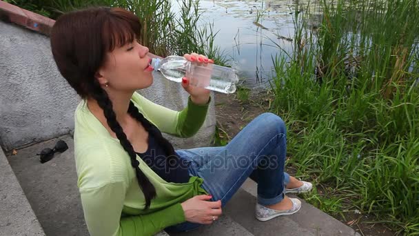 Bella ragazza seduta e bottiglia d'acqua potabile nel parco — Video Stock