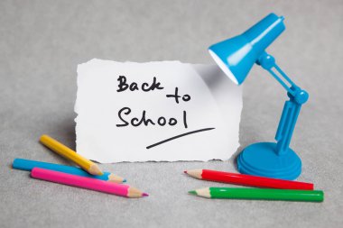 Geri okul kelime için küçük lamba ve kalem ile gri arka plan üzerinde