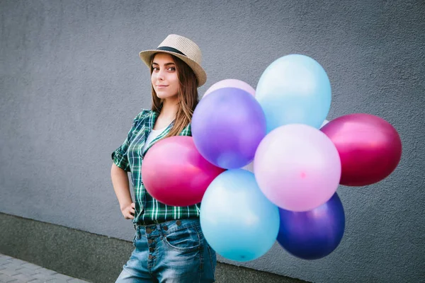 Lykkelig ung kvinde i plaid skjorte og hat stående med balloner - Stock-foto