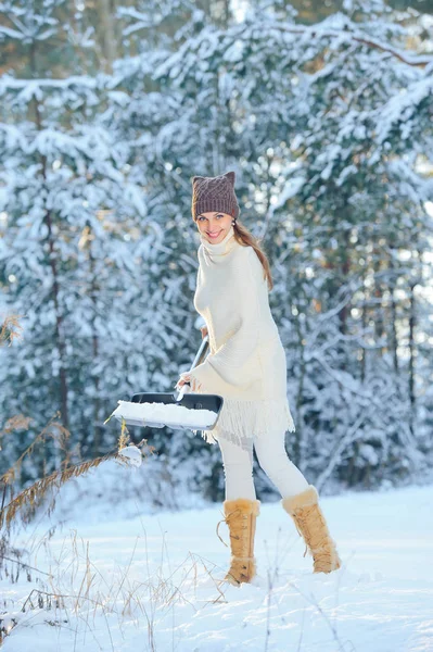 Женщина на фоне зимнего леса с лопатой убирает снег в морозный и солнечный день — стоковое фото