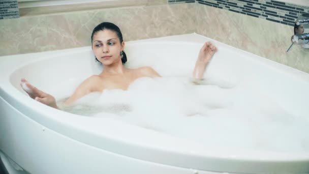 Девушка в пенной ванне расслабляется и опускается в воду — стоковое видео