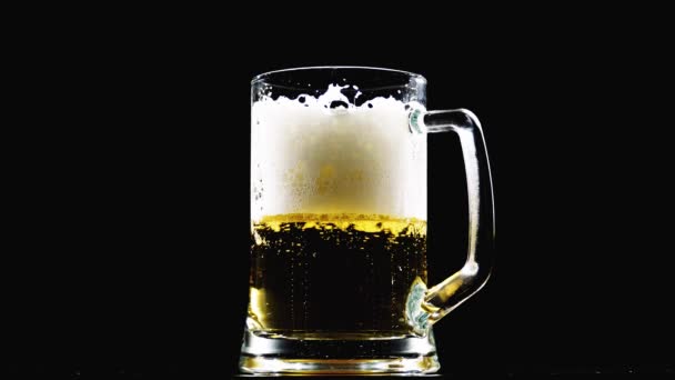Bier ergießt sich in ein Glas auf schwarzem Hintergrund. Zeitlupe — Stockvideo