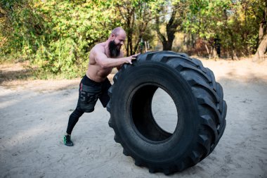 Muscular man working out with heavy tire  clipart