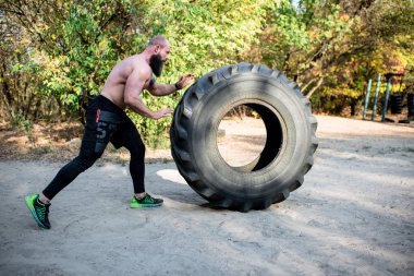 Bearded man exercising with tractor tire clipart