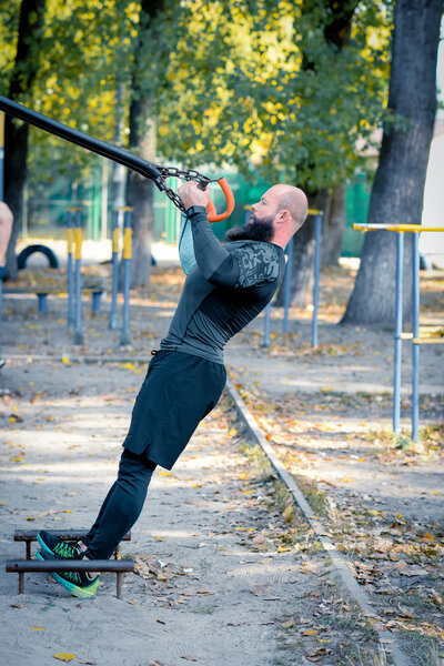 Muscular bearded man training with straps