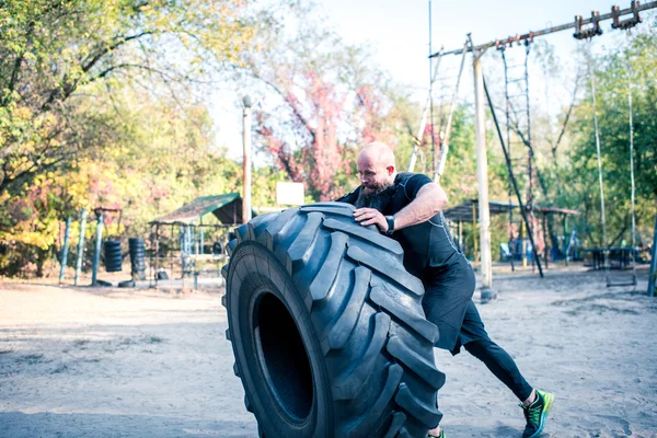 Man with beard lifting tractor tire — Stock Photo