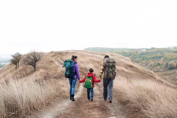 Family with backpacks walking on rural path — ストック写真