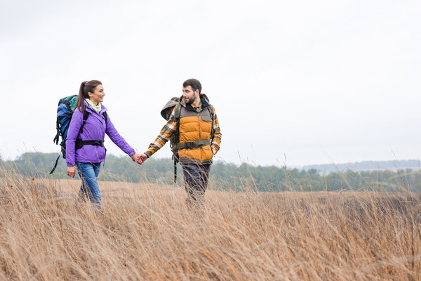 Smiling couple with backpacks walking in grass 