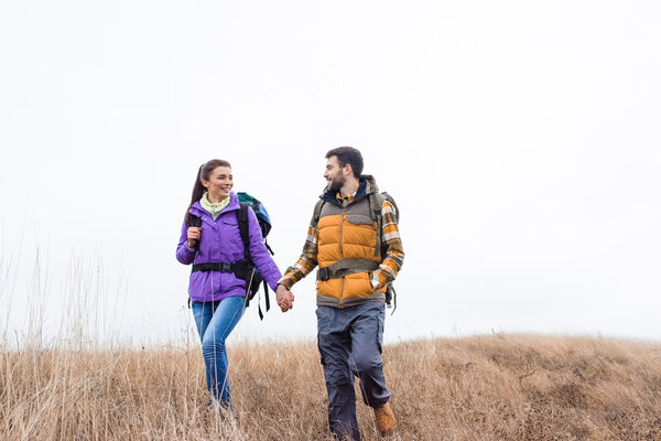 Smiling couple with backpacks walking in grass 