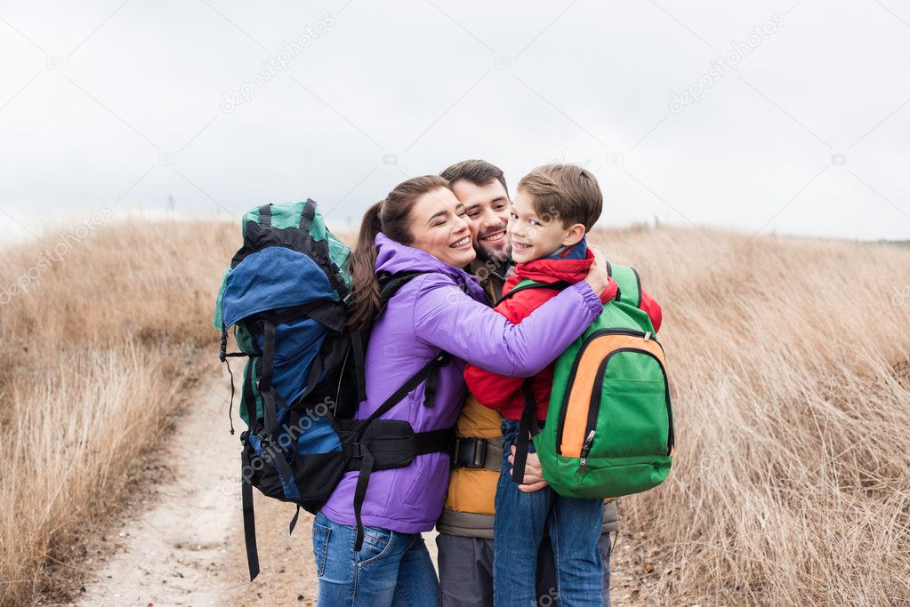 Happy family with backpacks hugging 