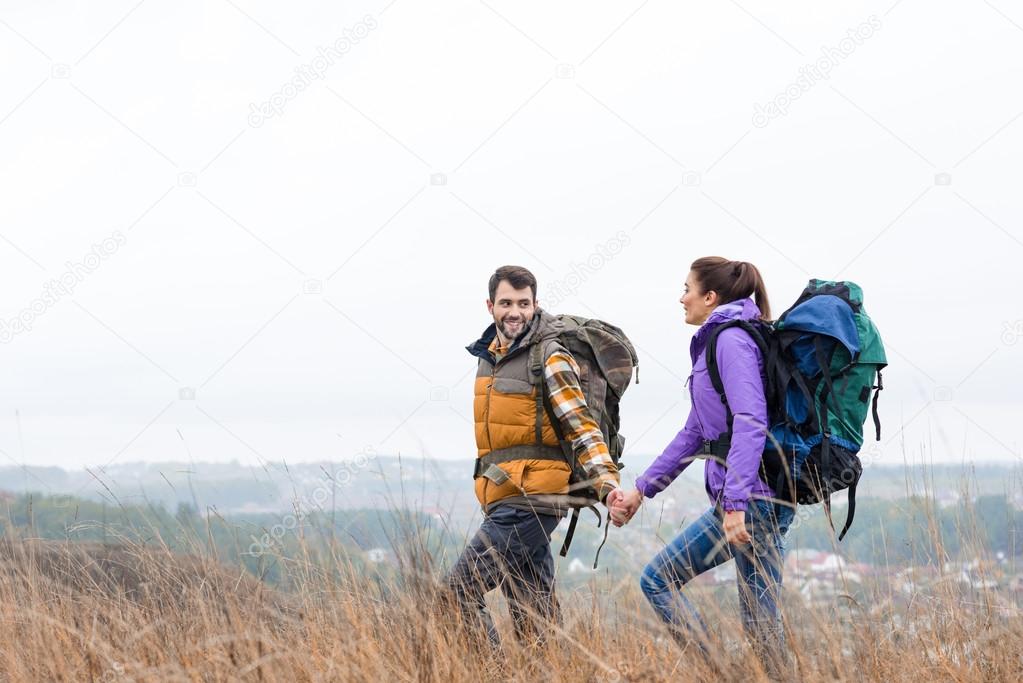 Smiling couple with backpacks walking in grass 